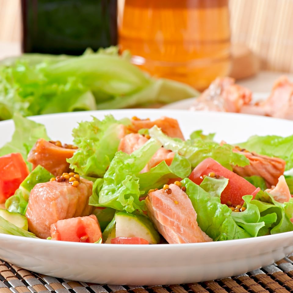 Zaca Salad with fresh lettuce, salmon, tomatoes, and mustard seeds in a white bowl.