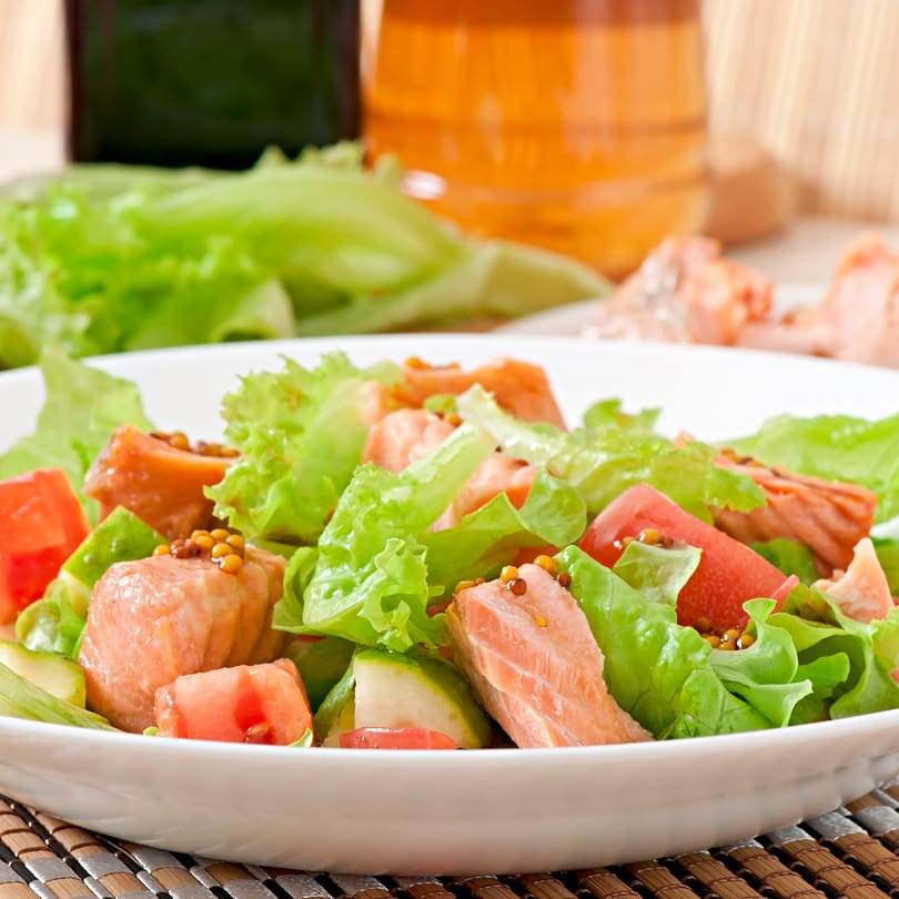 Zaca Salad with fresh lettuce, salmon, tomatoes, and mustard seeds in a white bowl.