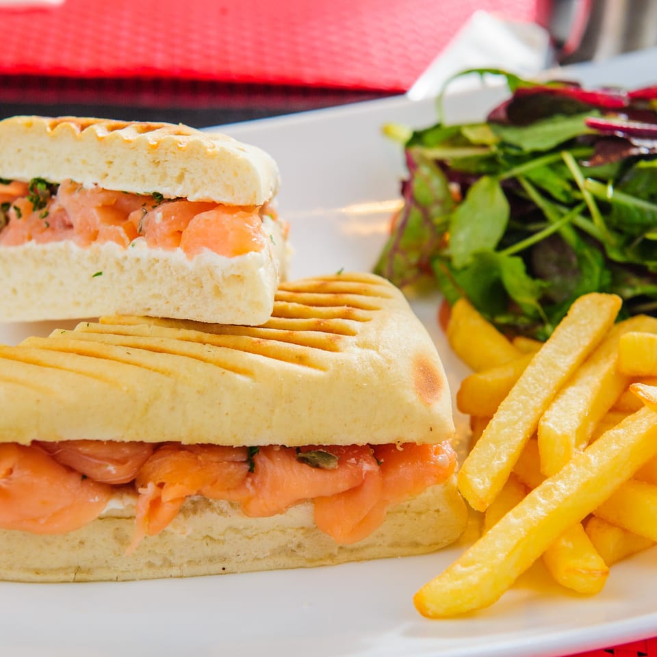 Grilled salmon panini with a side of french fries and a fresh green salad.