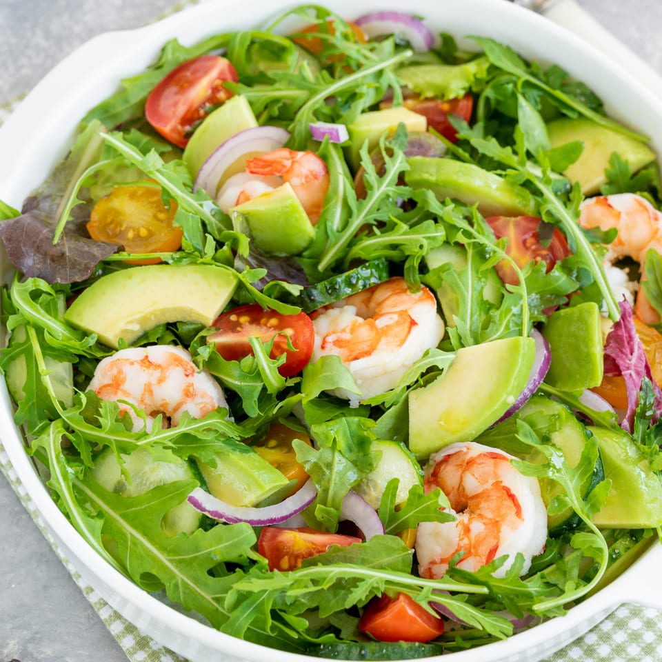 A vibrant Zaca Salad with shrimp, avocado, cherry tomatoes, red onion, and arugula in a white bowl.