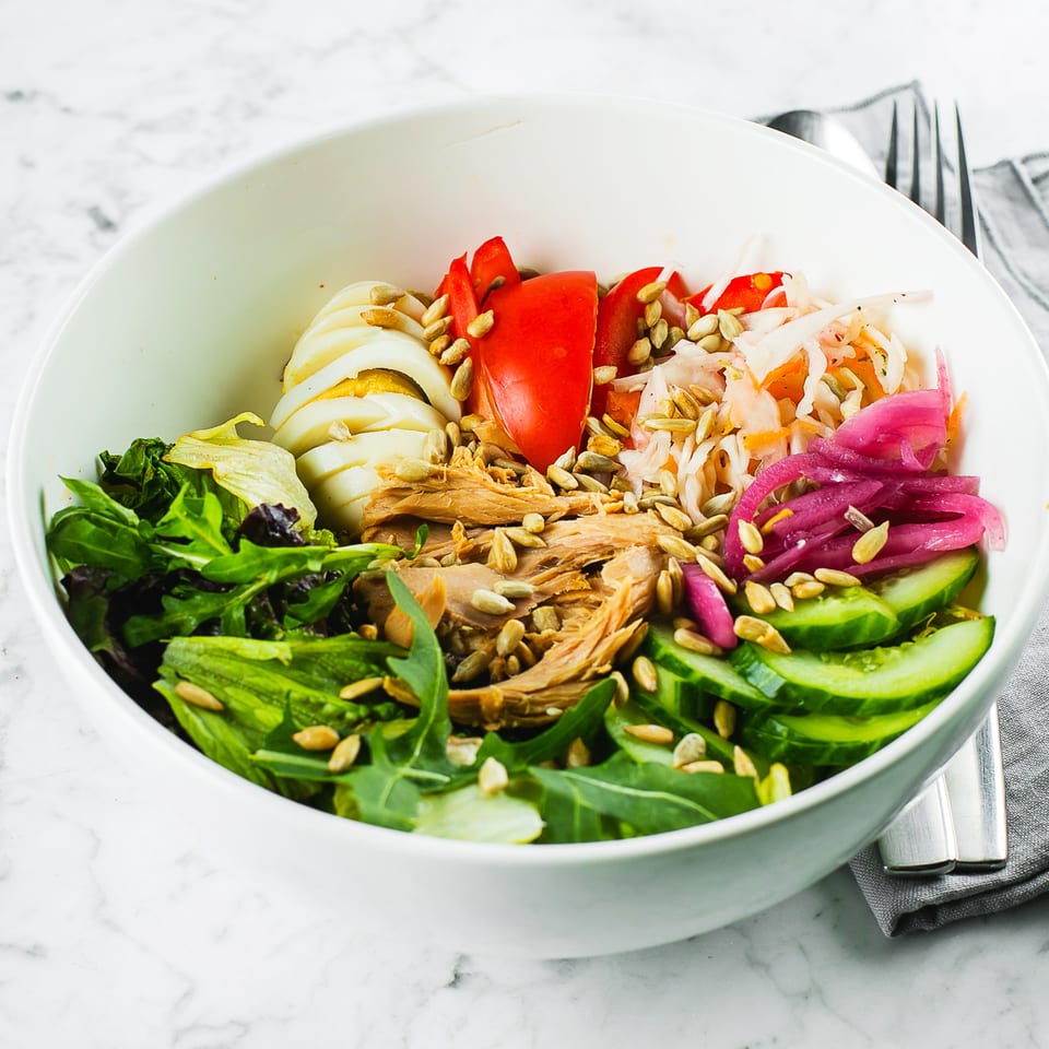 A Zaca Salad bowl with tuna, hard-boiled eggs, mixed greens, cucumbers, tomatoes, and pickled onions.