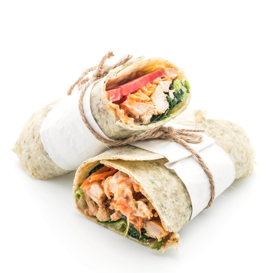Two Zaca Salad wraps, one cut in half, filled with chicken, lettuce, carrots, and tomatoes.